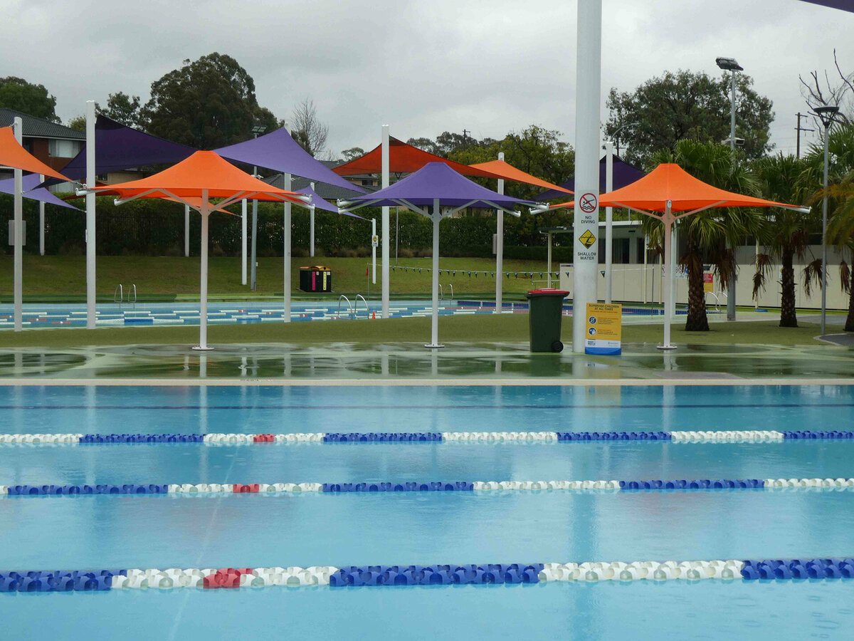 Purple and orange umbrella shade sails cover a grass patch in between swimming pools