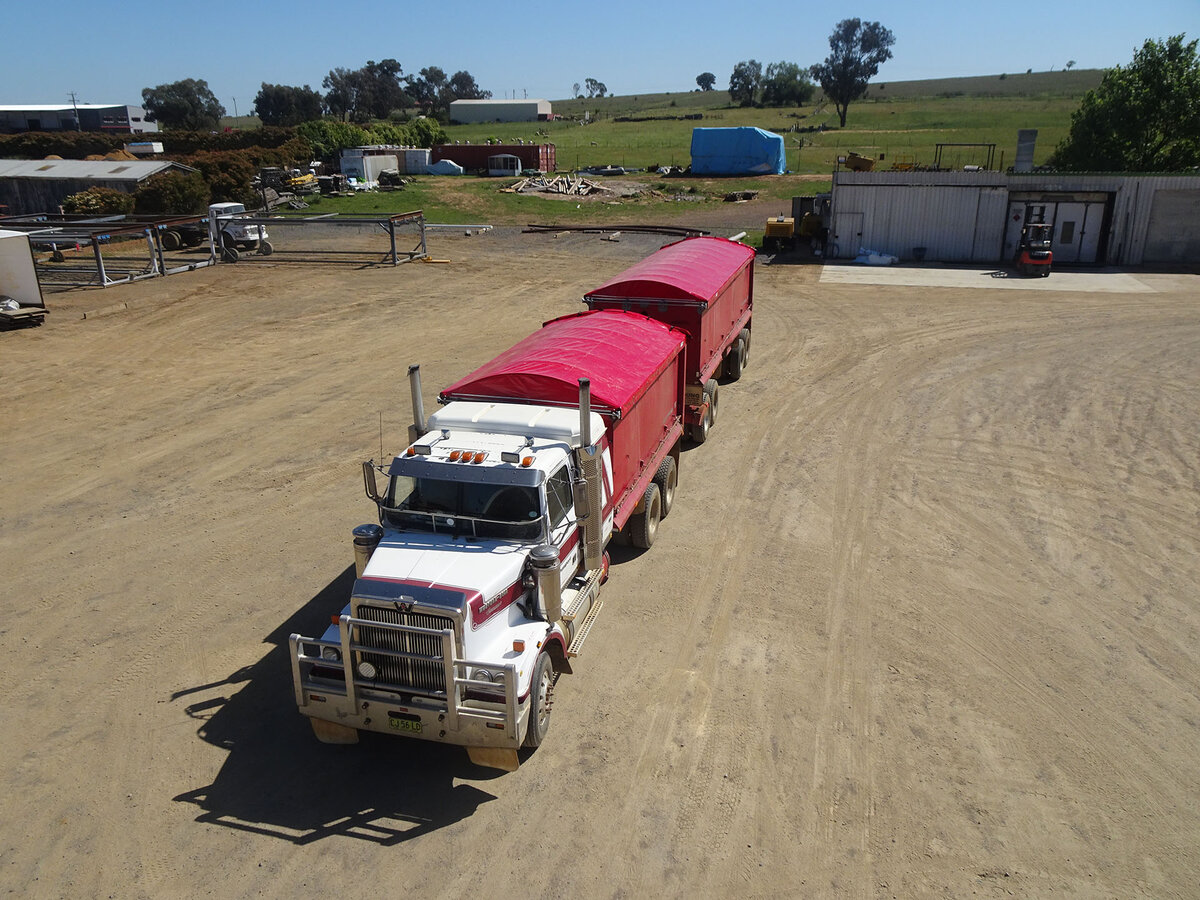 Truck and trailer in a dirt yard with a red retractable tarp on each trailer