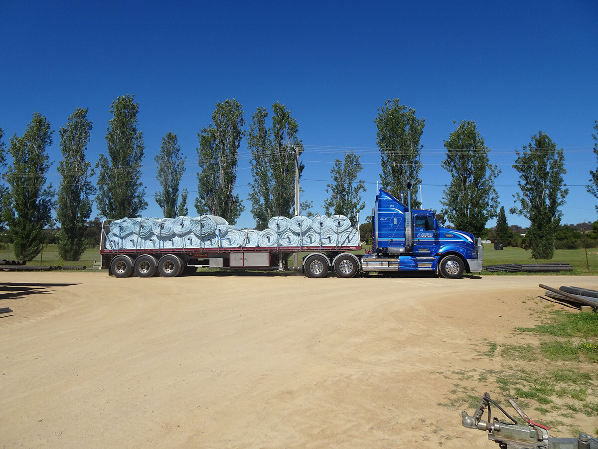 Grain bunkers loaded on a truck ready for delivery. The truck is parked on a dirt road. Tall skinny trees line one side of the road