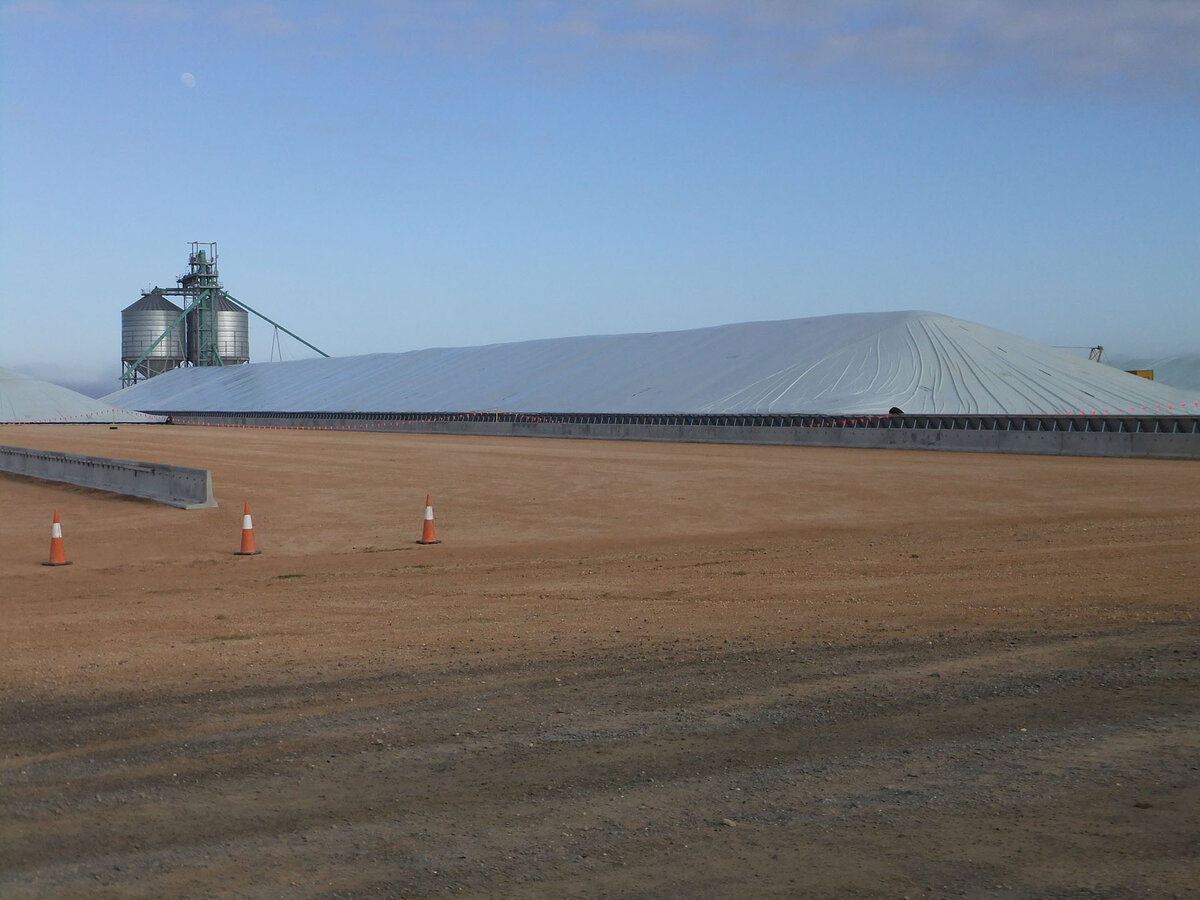 Large grain bunkers in a gravel area. Grain silos connect to the ends of each