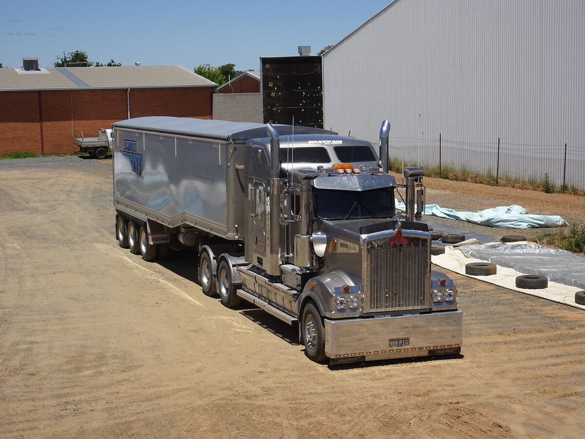 A grain truck is parked on a dirt driveway outside a large shed.