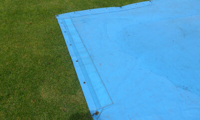 Corner of a blue cricket pitch cover on the grass