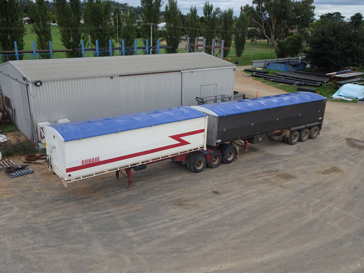 Two trailers parked next to a shed, both with blue roll over tarps