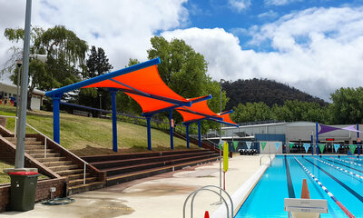 Red cantilever shade sails lining he edge of a swimming pool