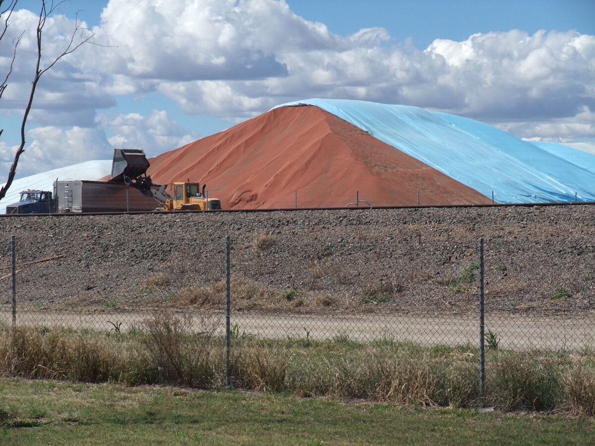 Stored grain bunker partially uncovered. A truck is parked waiting to be loaded.