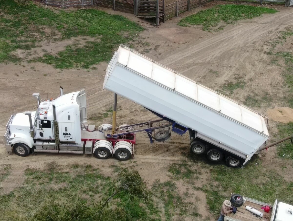 A white truck is on a dirt road. The trailer is being tilted backwards.