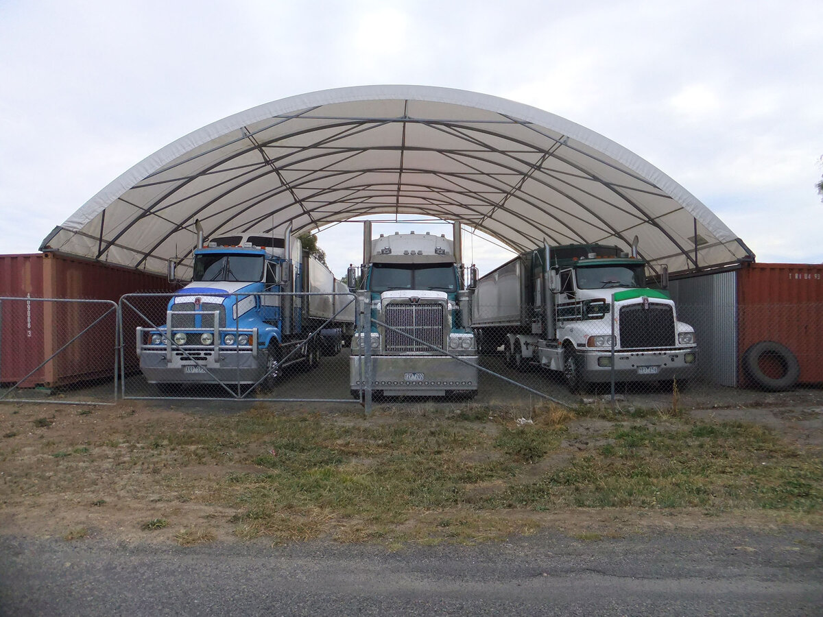 Three trucks parked under a large shelter spanning between two containers.