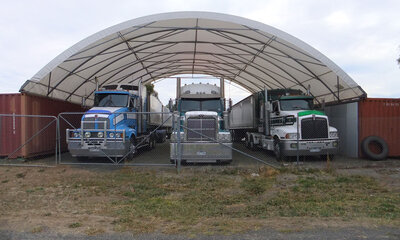 Three trucks parked under a large shelter spanning between two containers.