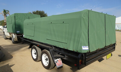 A ute carrying a trailer. The Ute tray and trailer both have green canvas covers attached