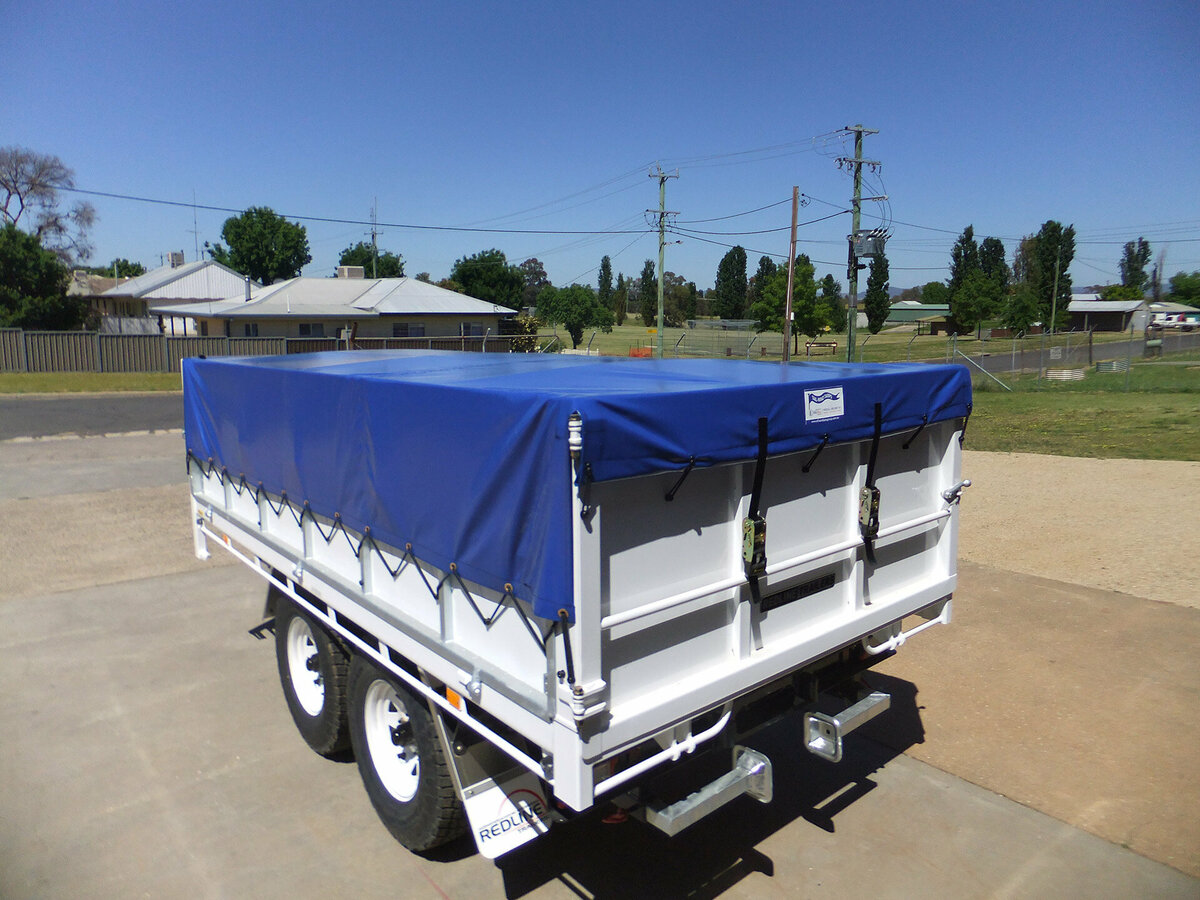 A trailer parked in a driveway with a blue canvas cover attached