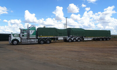 Truck and trailer parked in a dirt year, covered with a green truck tarp
