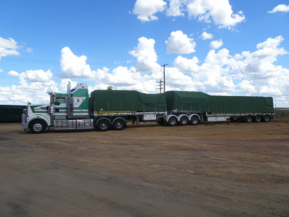 Truck and trailer parked in a dirt year, covered with a green truck tarp